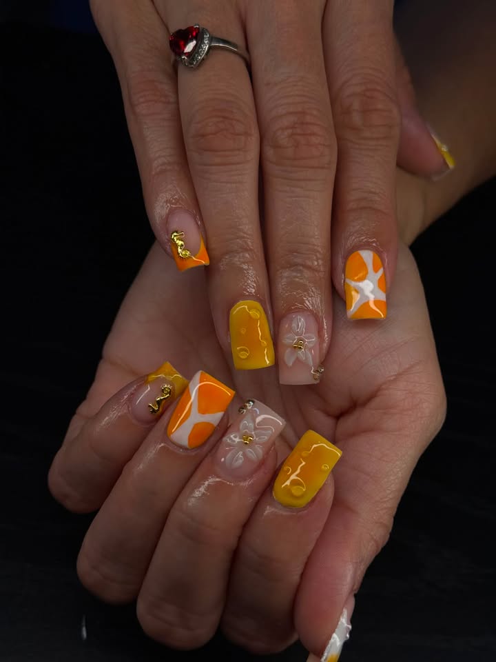 Orange and yellow manicure with white floral nail art and gold details
